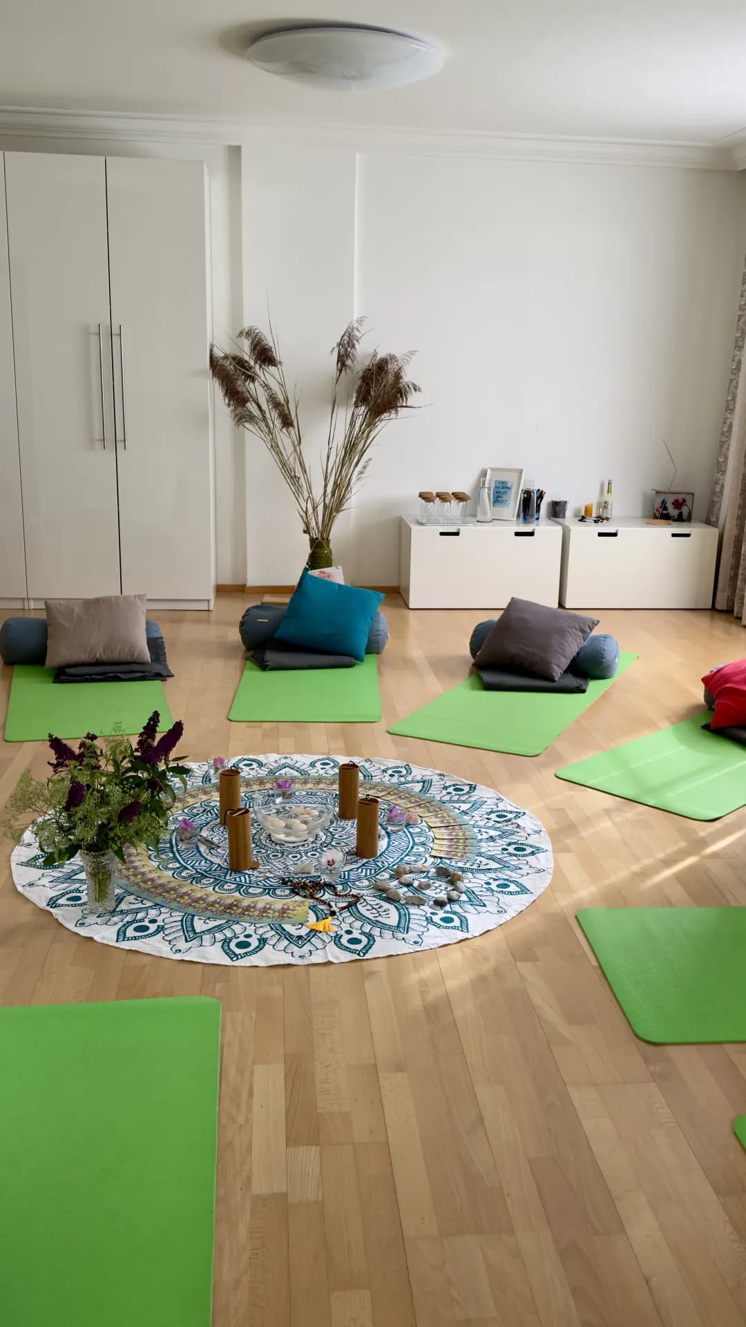 Heller Gruppenraum mit Yogamatten, Kissen und Blumen